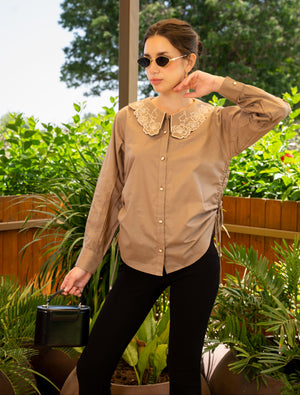 Woman wearing a beige blouse with a lace collar outdoors