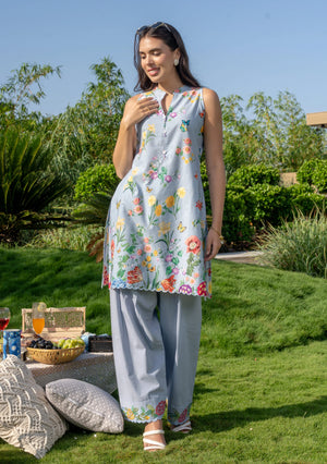 Woman in a floral outfit standing outdoors with greenery and a table in the background