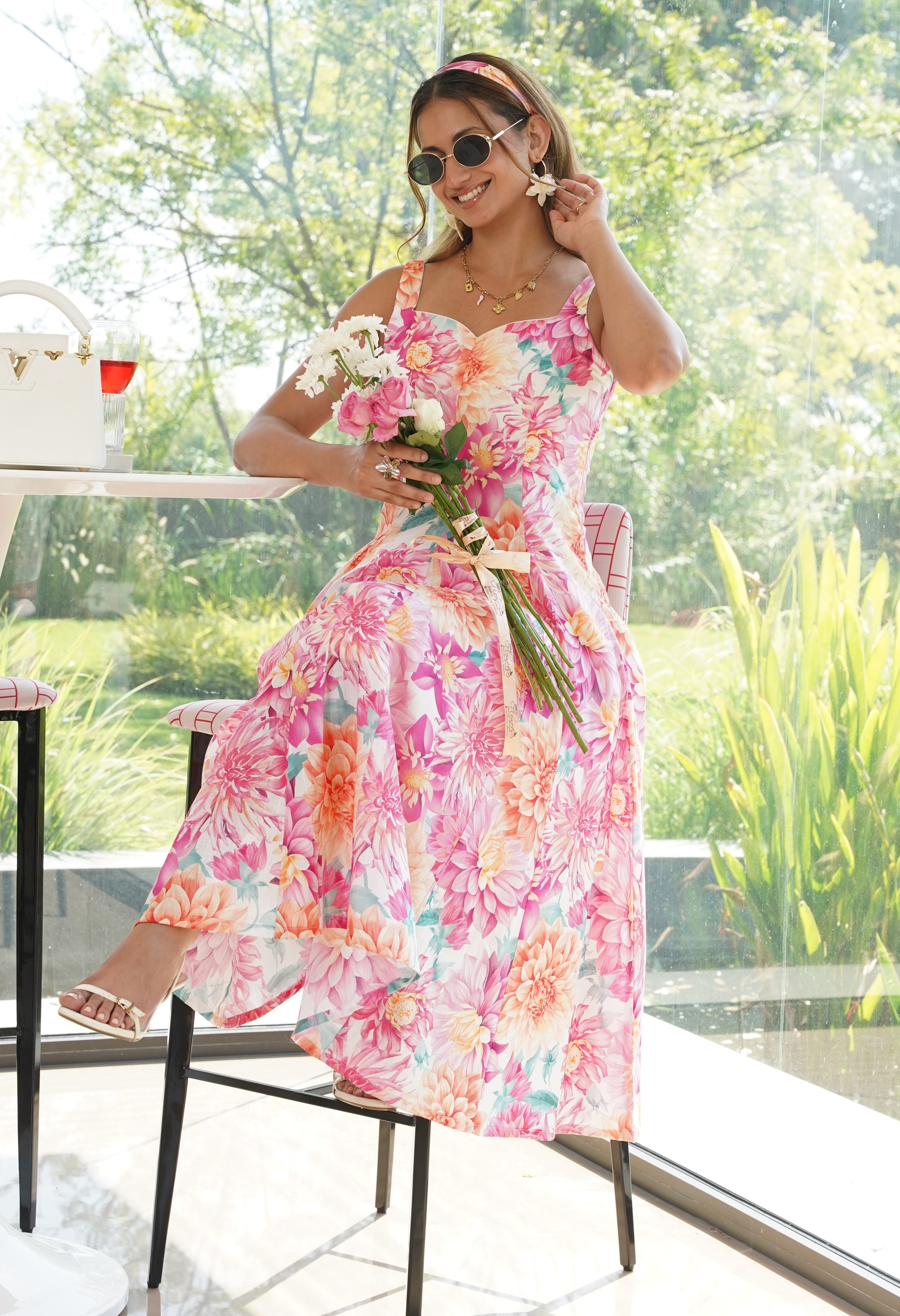 Woman in a colorful floral dress holding flowers indoors.