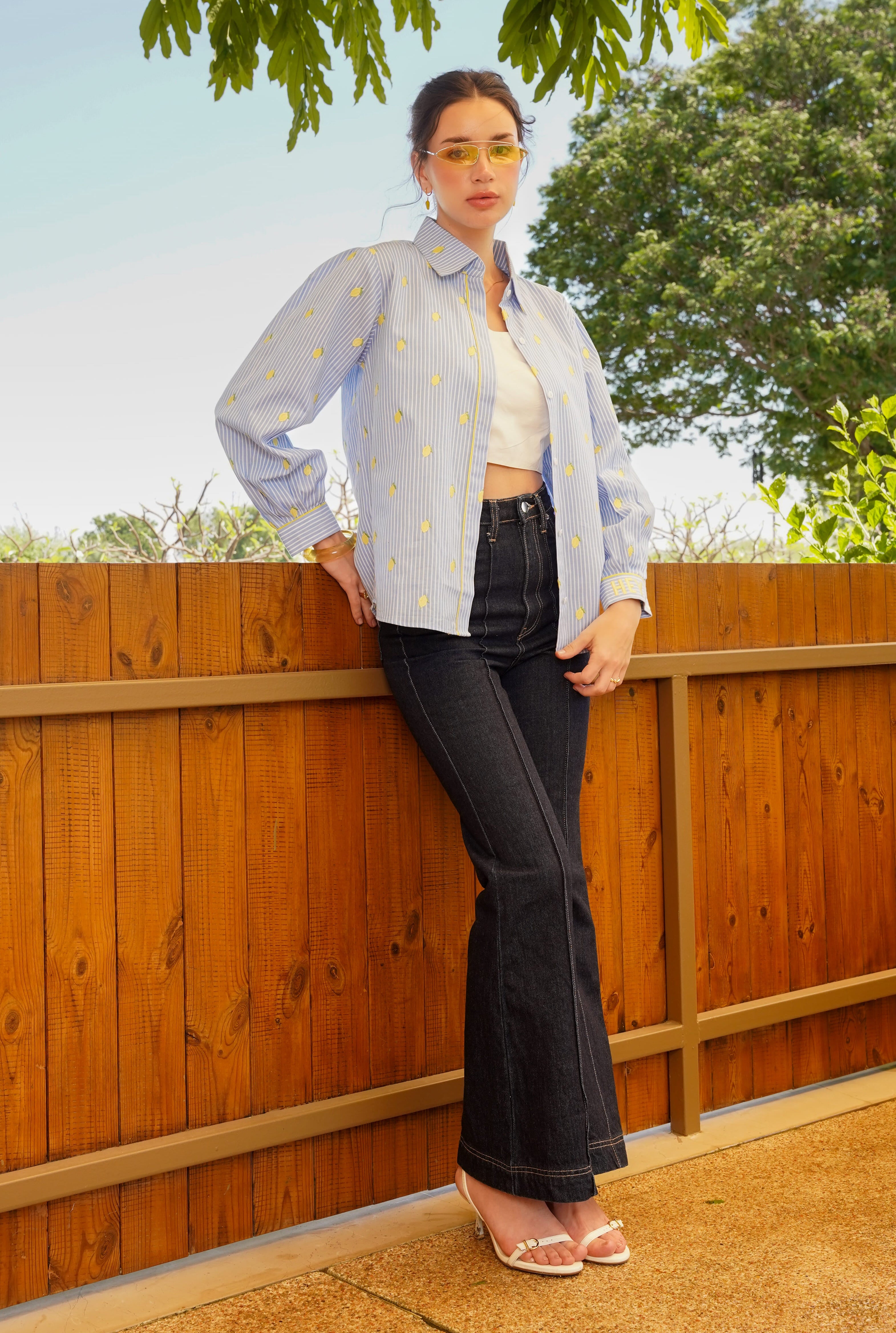Person standing outdoors by a wooden fence with trees in the background