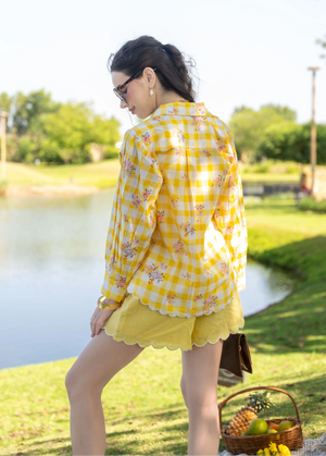 Woman in a yellow checkered shirt and shorts standing by a lake with a picnic basket.