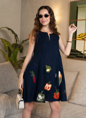 Woman wearing a navy dress with colorful vegetable patterns in a living room.